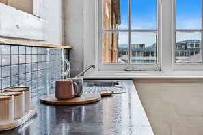 A kitchen with a black countertop, a window with a view of buildings, and a faucet. - Portsea - Heritage apartment by Salamanca (Battery Point)