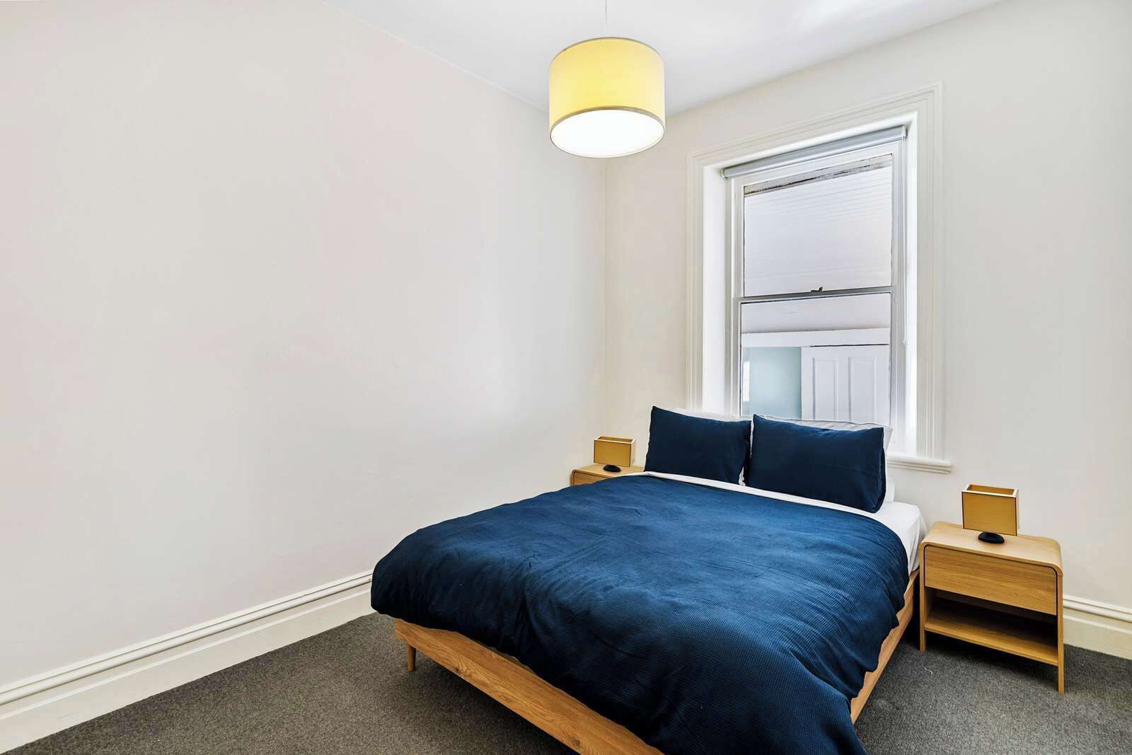 Een slaapkamer met een bed, twee nachtkastjes, een raam met zonwering en een hanglamp.