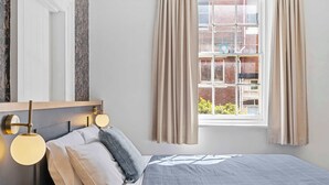 A neatly made bed with a blue and white checkered bedspread, a wooden headboard, and two wall-mounted light fixtures. - Portsea Place - Chic queen studio and parking (Battery Point)