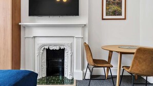 Una sala de estar con chimenea, televisor montado y un cuadro de un paisaje.