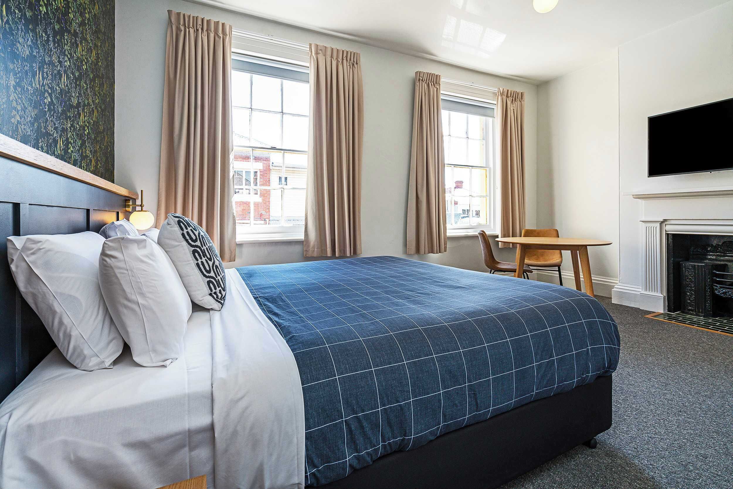 A hotel room with a bed, a TV, a fireplace, and a window with curtains.