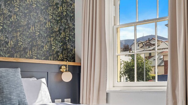 Een slaapkamer met een groot bed, een raam met gordijnen, een bloemenpatroon op de muur en uitzicht op gebouwen.