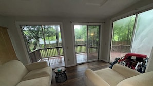 Una sala de estar con dos sofás beige, una mesita redonda y un ventanal corredizo que da a una terraza de madera.