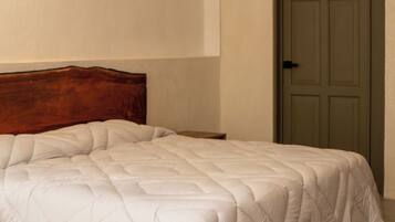 A bedroom with a large bed, a wooden headboard, a door, and a patterned floor.