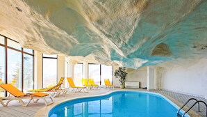 An indoor swimming pool with clear blue water, surrounded by sun loungers and a potted plant.