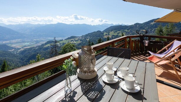 A wooden deck with a table set for tea, overlooking a mountainous landscape.