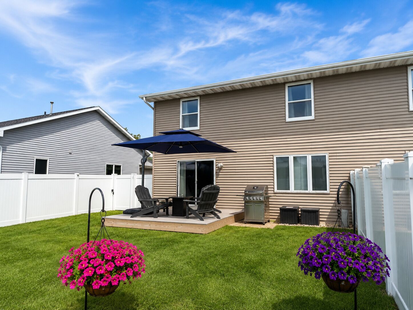 A residential backyard with a patio, outdoor furniture, and hanging flower planters.