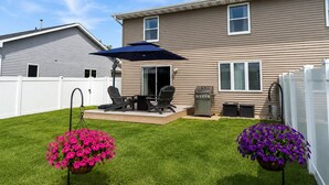 A residential backyard with a patio, outdoor furniture, and hanging flower planters.