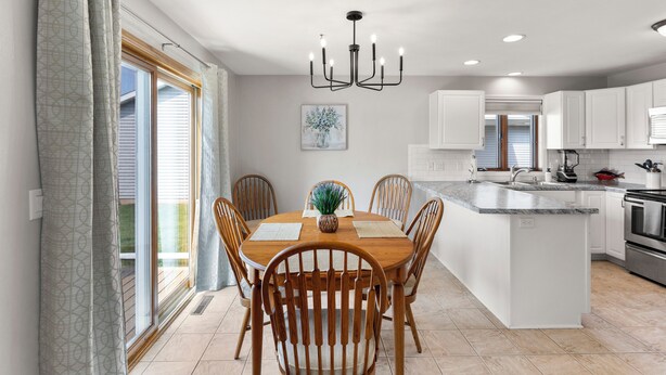 A modern kitchen with a central island, white cabinetry, and a dining area with wooden chairs and a table.