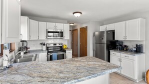 A modern kitchen with white cabinets, granite countertops, stainless steel appliances, and a coffee bar area.