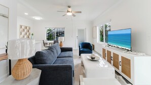 A modern living room with a grey sofa, a white coffee table, a TV on a white cabinet, and a ceiling fan.