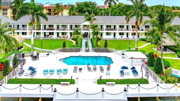 A hotel with a central swimming pool, multiple lounge areas, and a well-maintained garden.
