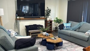 A living room with a flat-screen TV mounted on the wall, a sofa, a coffee table, and a small side table with a plant. - Cosy Coastal Cottage close to Maria Island Ferry - recently renovated (Triabunna)