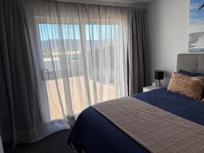 A hotel room with a bed, a nightstand, a lamp, and a view of the outdoors. - Cosy Coastal Cottage close to Maria Island Ferry - recently renovated (Triabunna)