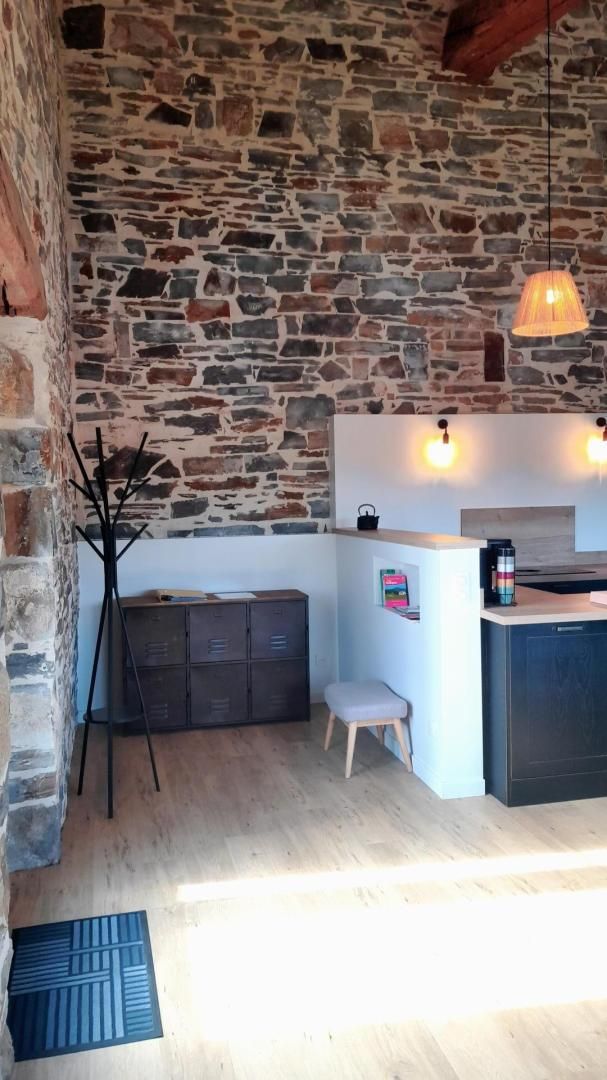 A cozy kitchen with a stone wall, wooden cabinets, a small stool, and pendant lighting.