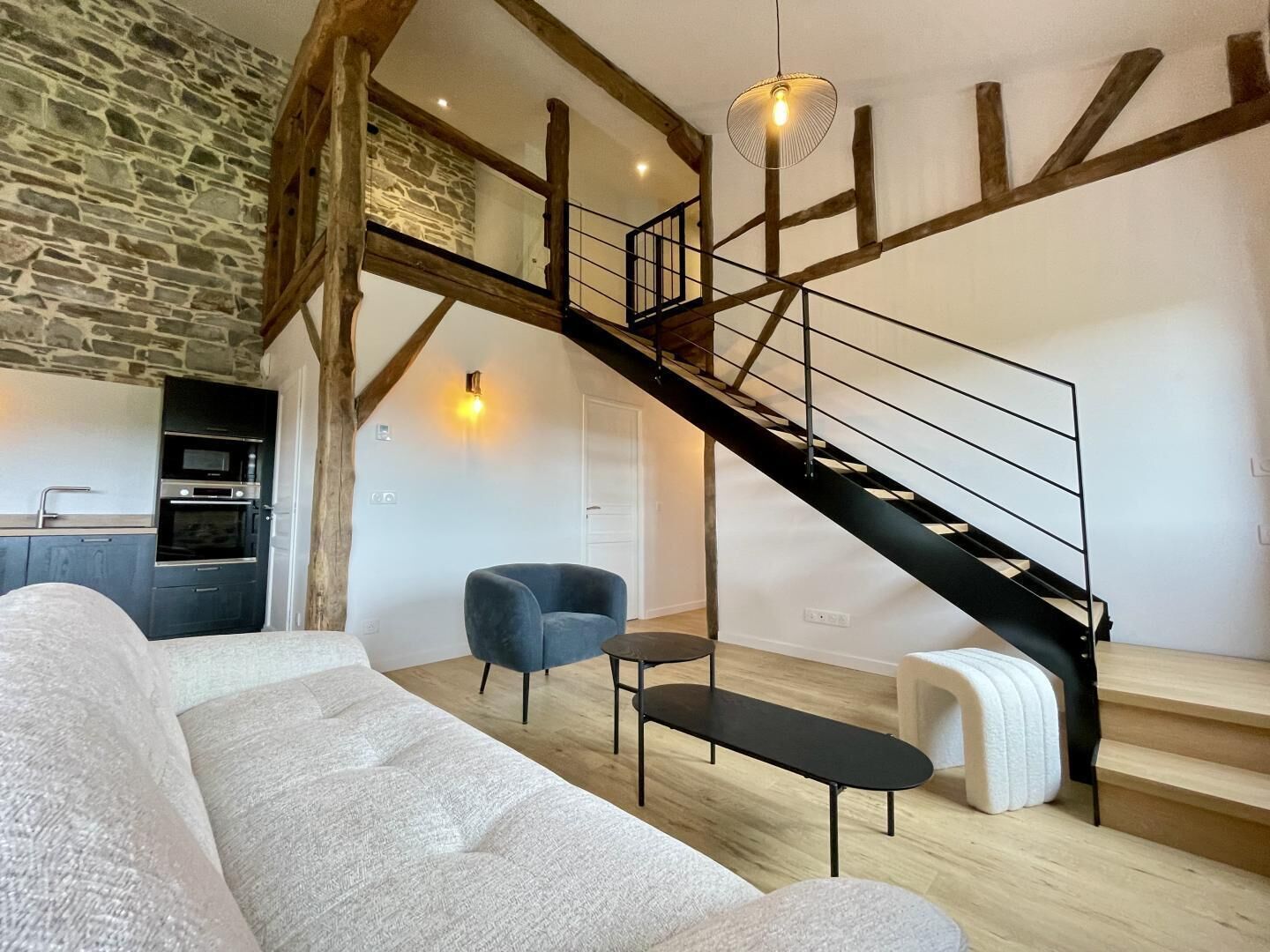 A modern living room with a stone wall, a black staircase, a sofa, a chair, and a small table.