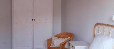 Un dormitorio con cama, una silla, una mesita y un armario.