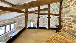 A spacious room with exposed wooden beams, stone walls, and a view through a window to the outside. - HARRIA - SAINT-PEE-SUR-NIVELLE (SAINT-PEE-SUR-NIVELLE)