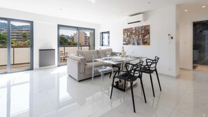 A spacious living area with a dining table, chairs, and a sofa. There are large windows providing a view of the cityscape. - Central 1-Br with Balcony – Rue d’Antibes, Cannes (Cannes)