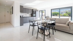 A modern kitchen with grey cabinets, a dining area with a glass table, and a sofa. - Central 1-Br with Balcony – Rue d’Antibes, Cannes (Cannes)