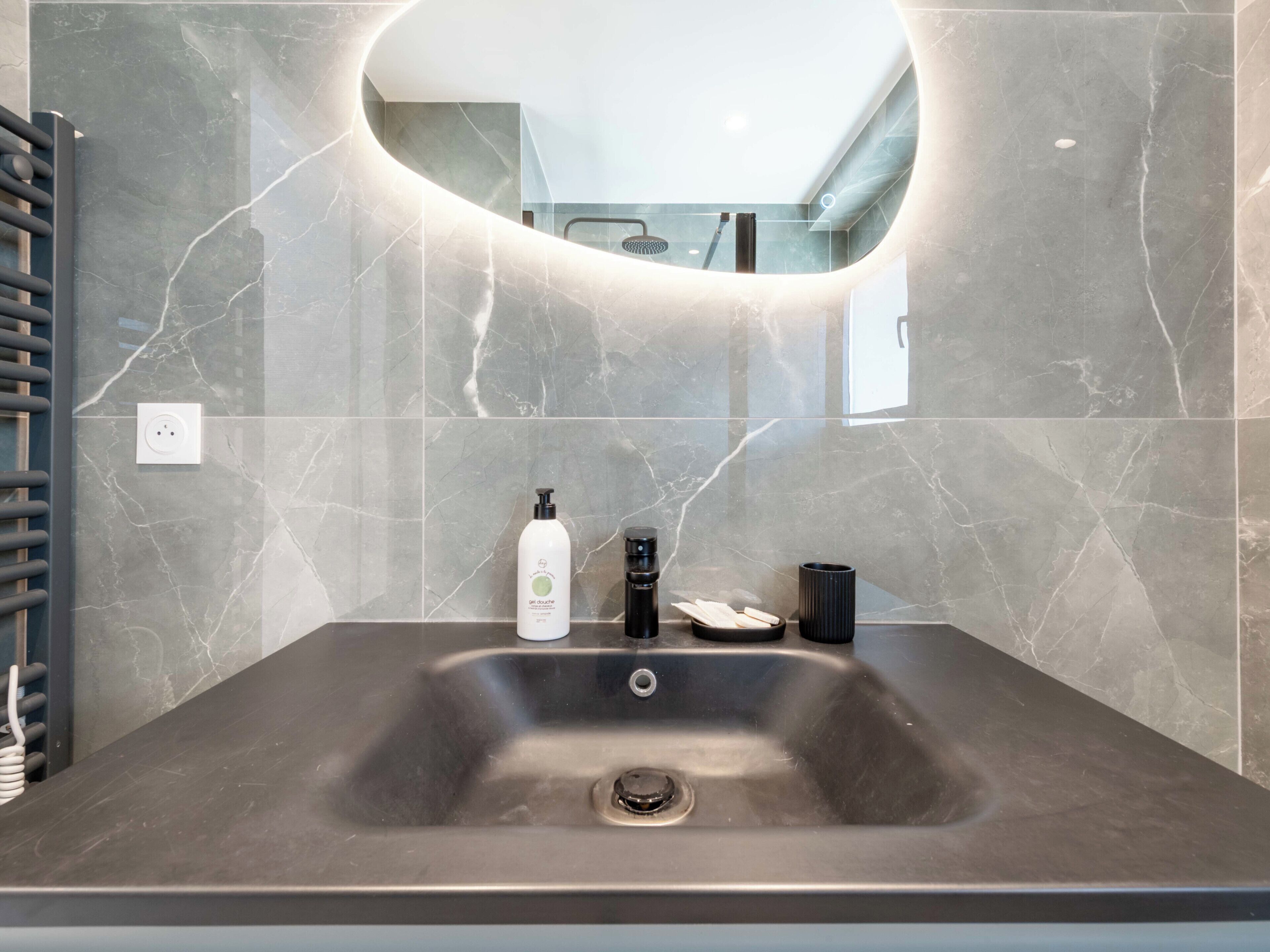 Een moderne badkamer met een grote wastafel, een spiegel en een douche die in de spiegeling zichtbaar is.