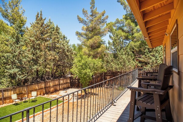 A wooden deck with chairs, a fenced yard, and tall trees.
