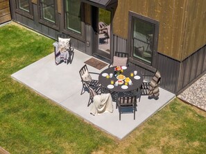 Une terrasse extérieure avec une table ronde et des chaises, un petit jardin et un bâtiment doté de grandes fenêtres.