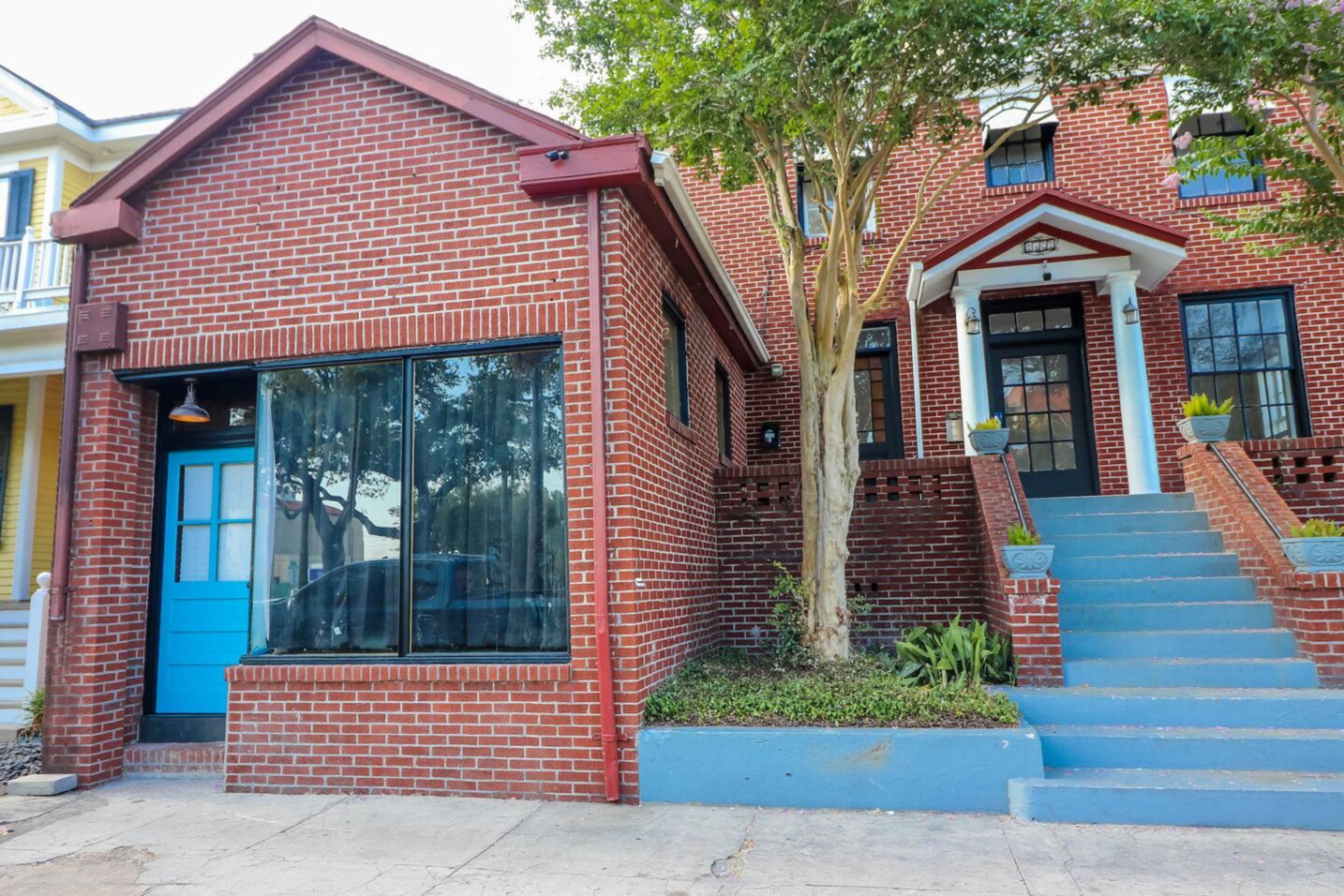 A red brick house with a blue door, large windows, and a tree in the front yard.
