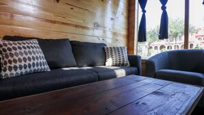 A wooden wall, a sofa with patterned pillows, a wooden coffee table, and a view of buildings through a window. - Restored Historic Loft - 3 Mins to the Beach (Galveston)