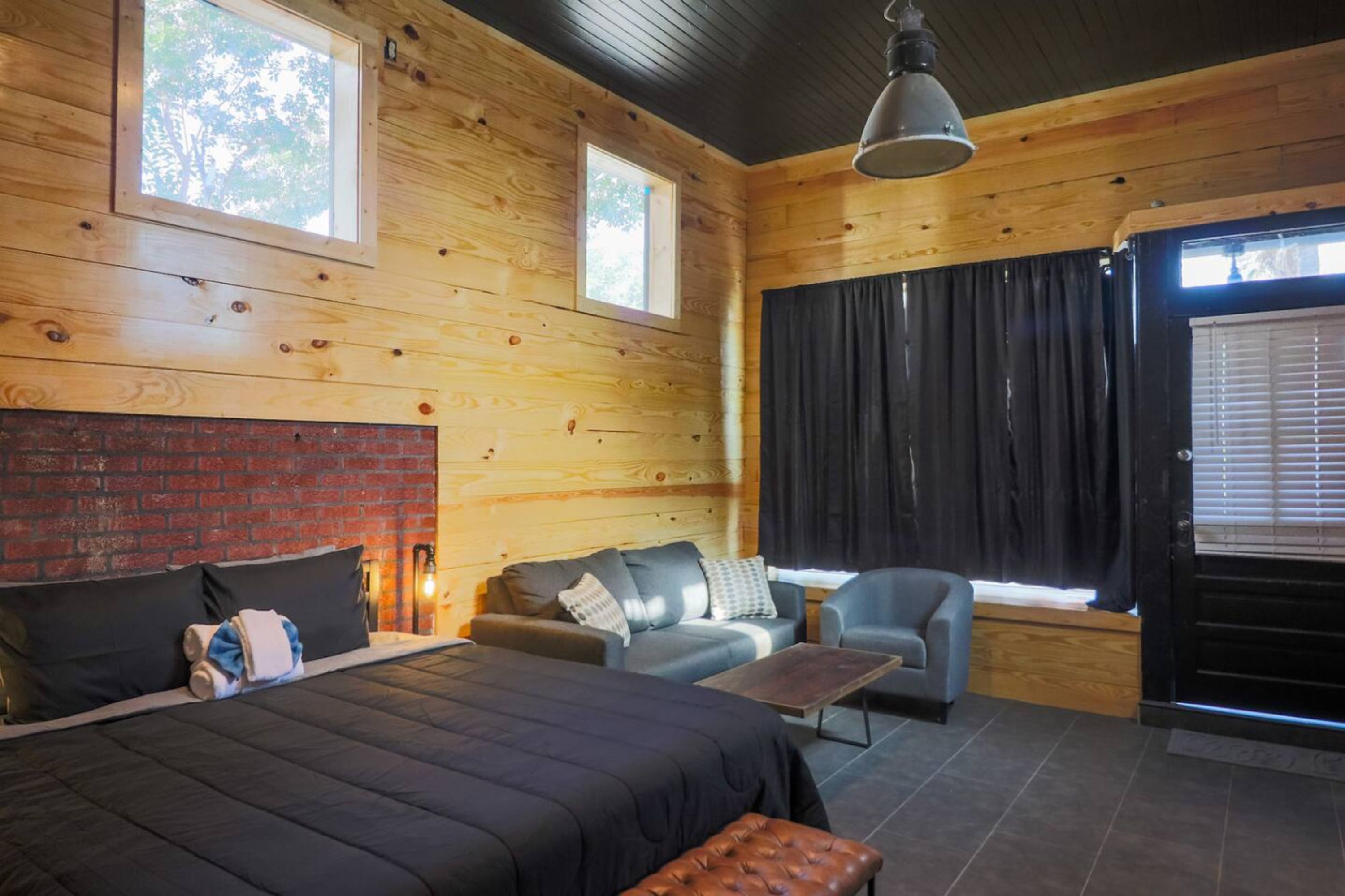 A wooden cabin room with a bed, two sofas, a table, and a window with curtains.