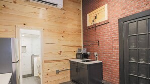 A compact kitchen with wooden walls, a black door, and a small countertop with a microwave. - Restored Historic Loft - 3 Mins to the Beach (Galveston)