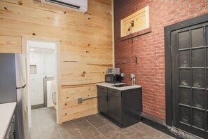 A compact kitchen with wooden walls, a black door, and a small countertop with a microwave. - Restored Historic Loft - 3 Mins to the Beach (Galveston)