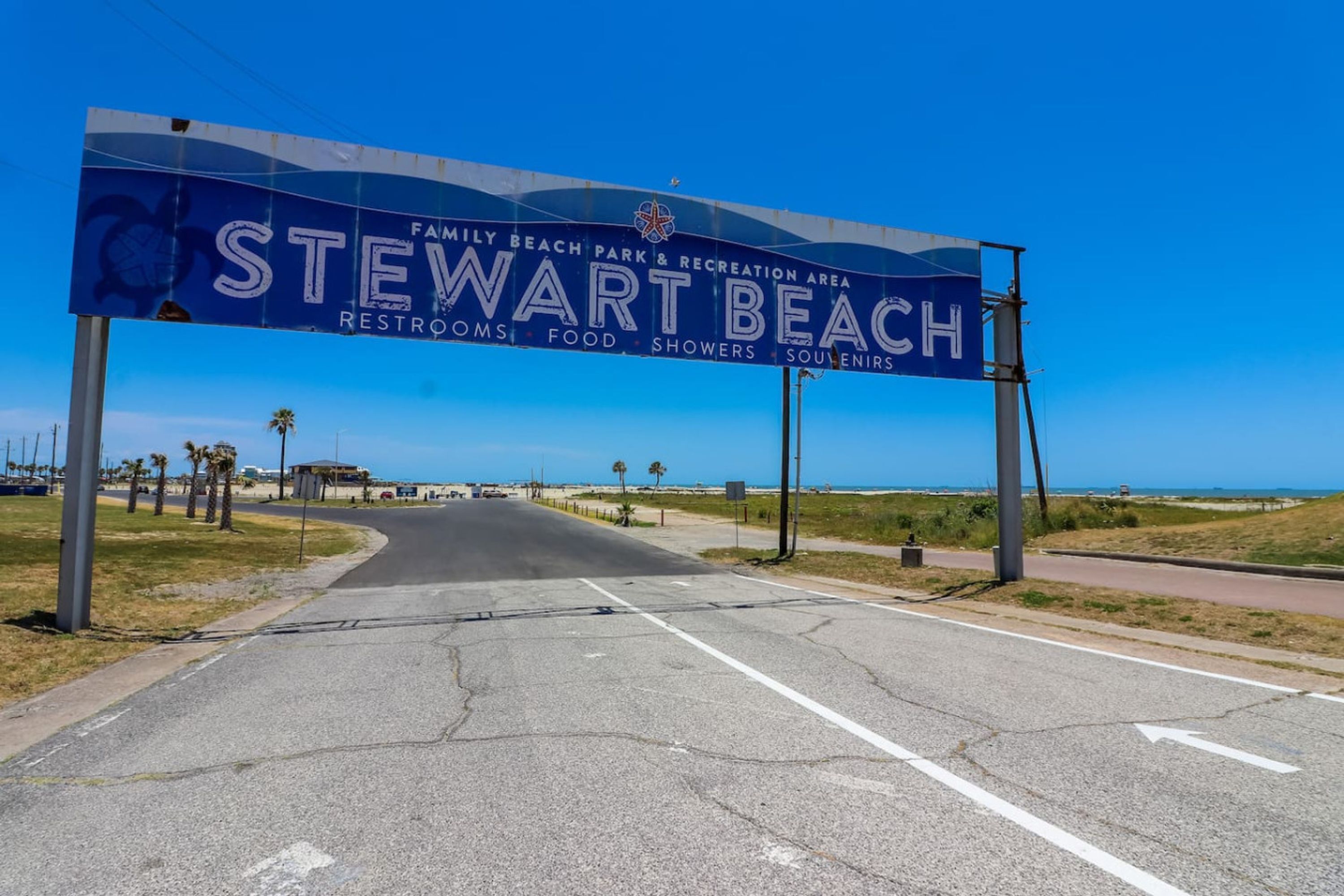 Une route menant à Stewart Beach, avec un grand panneau bleu indiquant un parc de plage familial et les commodités offertes dans la zone de loisirs.