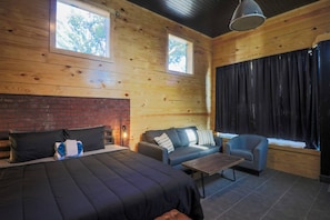 A log cabin room with a bed, sofa, armchair, and a fireplace. - Restored Historic Loft - 3 Mins to the Beach (Galveston)