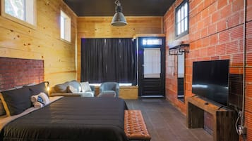 Um quarto rústico estilo cabana, com uma cama, duas cadeiras, um banco, uma televisão e uma janela com cortinas.