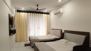 A hotel room with two beds, a ceiling fan, an air conditioning unit, and a window with curtains. - Karjat Poolside Studio | Pvt Balcony | Couples, Friends & Family | Near Mumbai (Karjat)