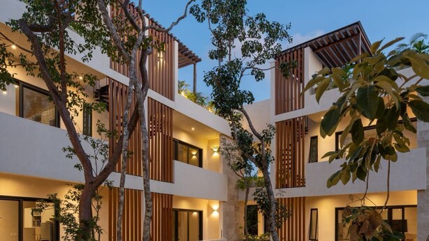 Un hotel de varios pisos con piscina en un patio central, rodeado de exuberante follaje y árboles.
