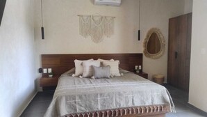 Un dormitorio ordenado con cama, mesitas de noche, aire acondicionado de pared y un tapiz de macramé.