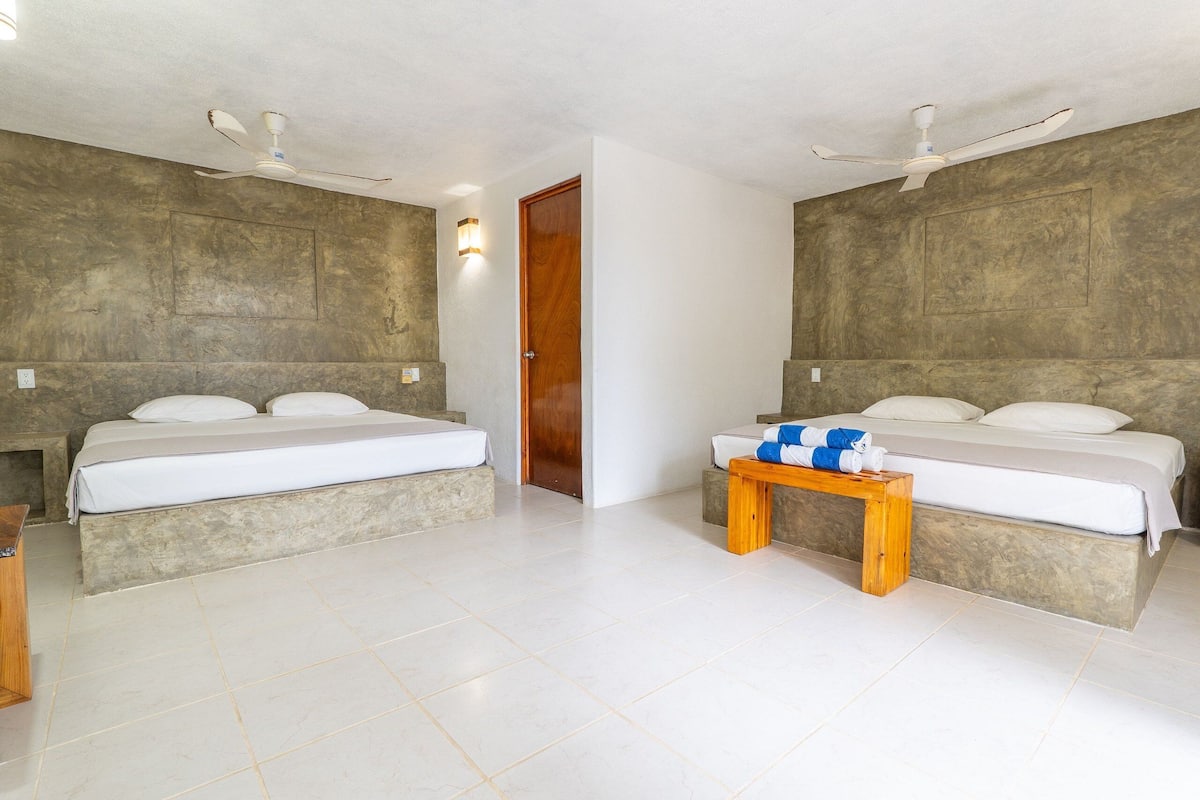 A hotel room with two beds, a wooden nightstand, and ceiling fans.