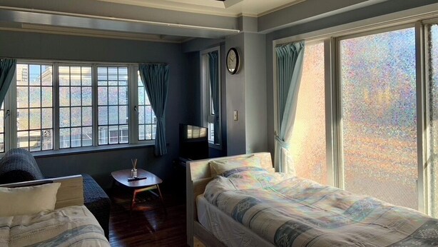 A room with a bed, a chair, a small table, and a window with curtains.