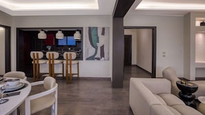 A modern living room with a dining area, featuring a sofa, chairs, a dining table, and a bar area with a painting on the wall. - Nile Haven Zamalek Island 3BR (Cairo Governorate)