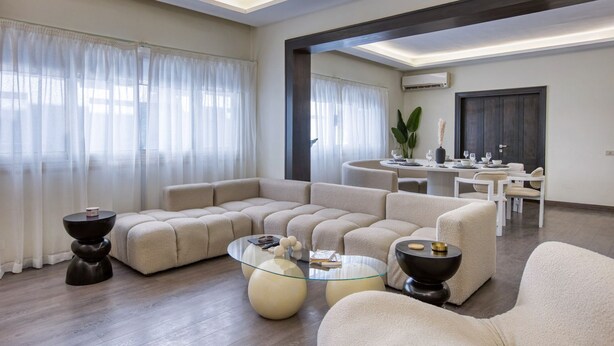 A modern living room with a sectional sofa, a glass coffee table, and a dining area in the background. - Nile Haven Zamalek Island 3BR (Cairo Governorate)