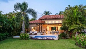 A house with a swimming pool, outdoor seating, and lush tropical landscaping.
