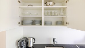 A kitchen with white cabinets, a sink, a coffee maker, and stacked plates and bowls. - Blueground | Basel-Vorstaedte, view, nr Rhine (Basel)