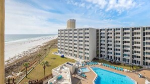 A hotel with multiple floors, a pool area with lounge chairs, and a beach view.