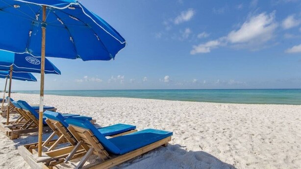 A beach with wooden lounge chairs and blue umbrellas.
