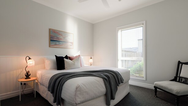 Ein Schlafzimmer mit Bett, Nachttischlampen, einem Sessel, einem Deckenventilator und einem Fenster mit Jalousien.