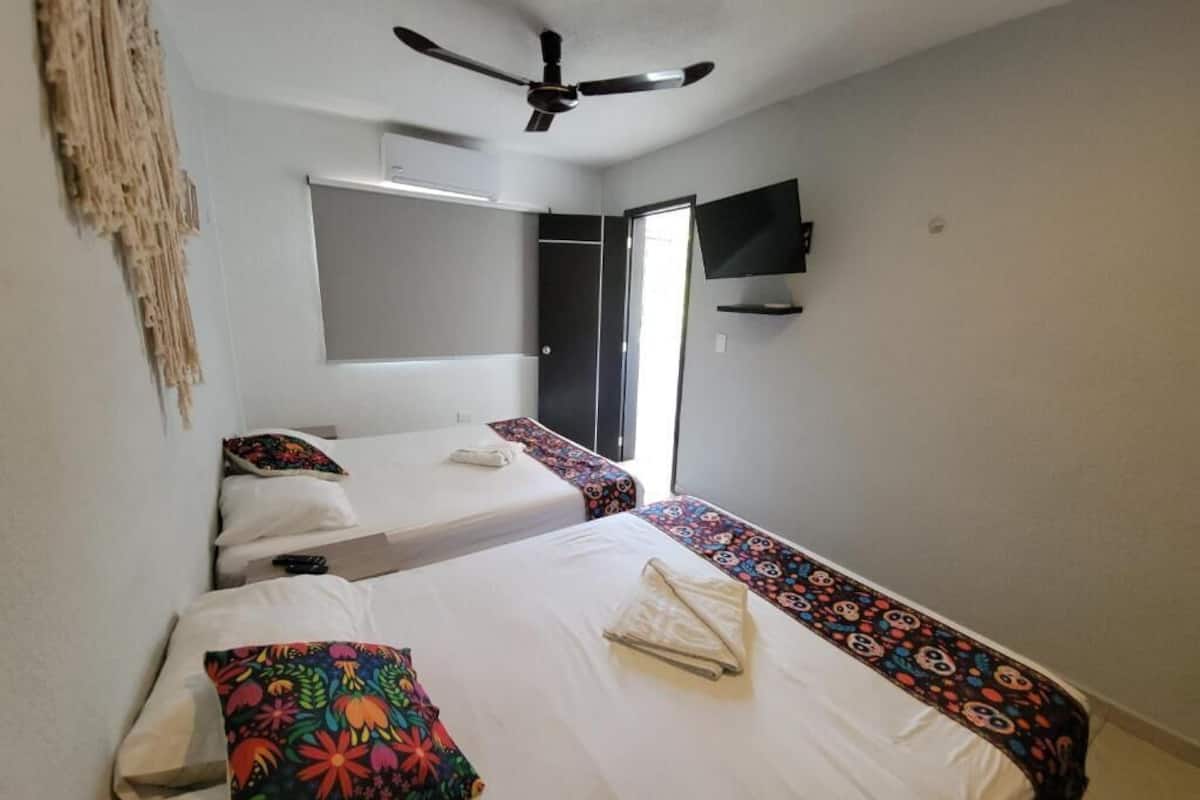 A hotel room with two beds, a ceiling fan, a flat-screen TV, and a window.