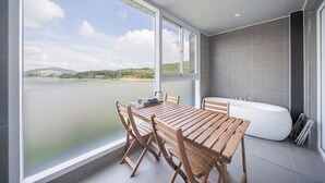 Un baño moderno con bañera, una mesa con sillas y un ventanal con vistas a un cuerpo de agua.