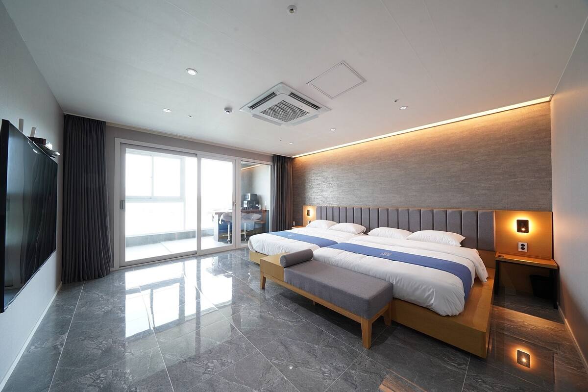 A modern hotel room with a large bed, a flat-screen TV, and a sliding glass door leading to a balcony.